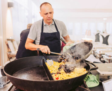 Koch mit einer riesen Pfanne und Paella darin