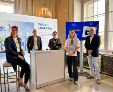 Personen vorm Shared Charging Stand lachen in die Kamera auf Oesterreichs Energie Kongress
